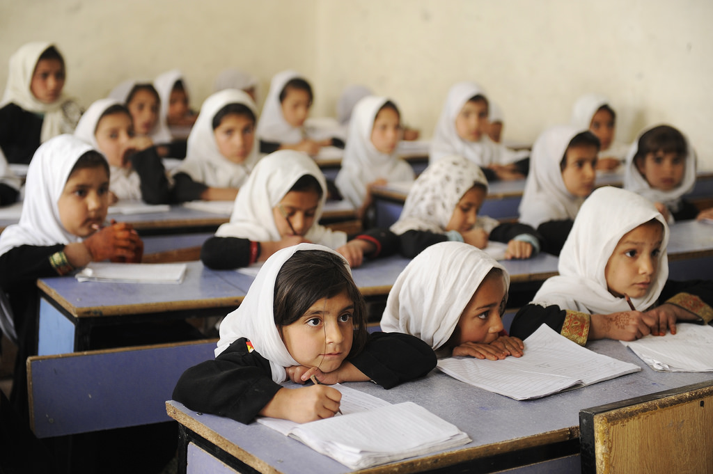 A depiction of young girls in a classroom, listening attentively to their teacher.